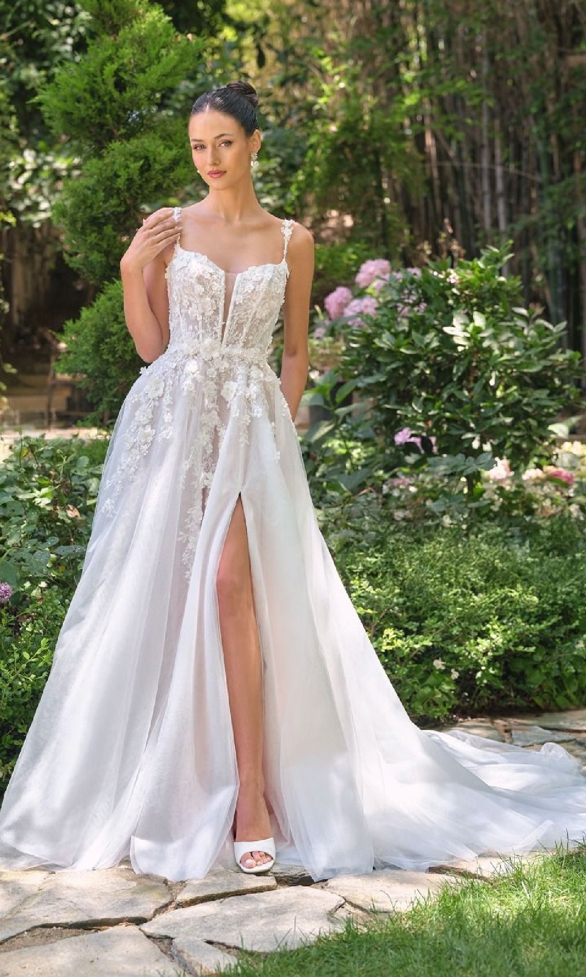 Woman in a white wedding dress standing outdoors with greenery in the background